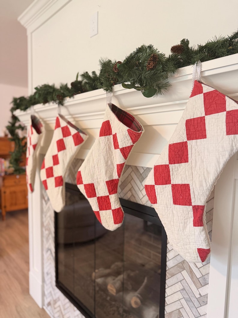 May include: Four quilted Christmas stockings hanging in a row, each featuring a red and white checkered pattern. The stockings are constructed with a visible stitched texture and have a red and black plaid fabric lining visible at the top opening.
