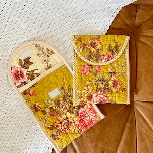 May include: Two quilted pot holders with a floral pattern in shades of yellow, pink, and green. The pot holders have a white and yellow checkered trim.