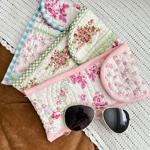 May include: A quilted floral fabric sunglasses case with a pink trim and a pair of gold aviator sunglasses with black lenses.