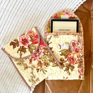 May include: A floral patterned quilted fabric case with a red and white checkered trim. The case is designed to hold an e-reader. The e-reader is visible inside the case and displays the text "WATER STREET".