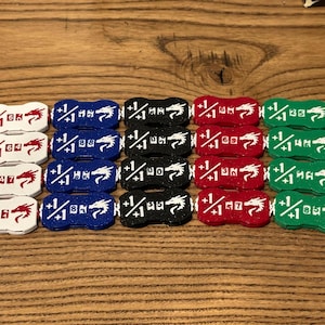 May include: A collection of twenty rectangular game tokens arranged in four rows and five columns. Each token features a white dragon icon, the text +1/+1, and a unique two-digit number. The tokens are colored white, blue, black, red, and green.