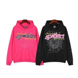 K&ouml;nnte beinhalten: Zwei lang&auml;rmelige Kapuzenpullover, einer in Pink und einer in Schwarz. Beide haben eine gro&szlig;e Grafik auf der Brust mit dem Wort spider! in pinker Schrift, einem Spinnennetz-Design, kleinen bunten Sternen und dem Text pangaia the punk bares the alien.
