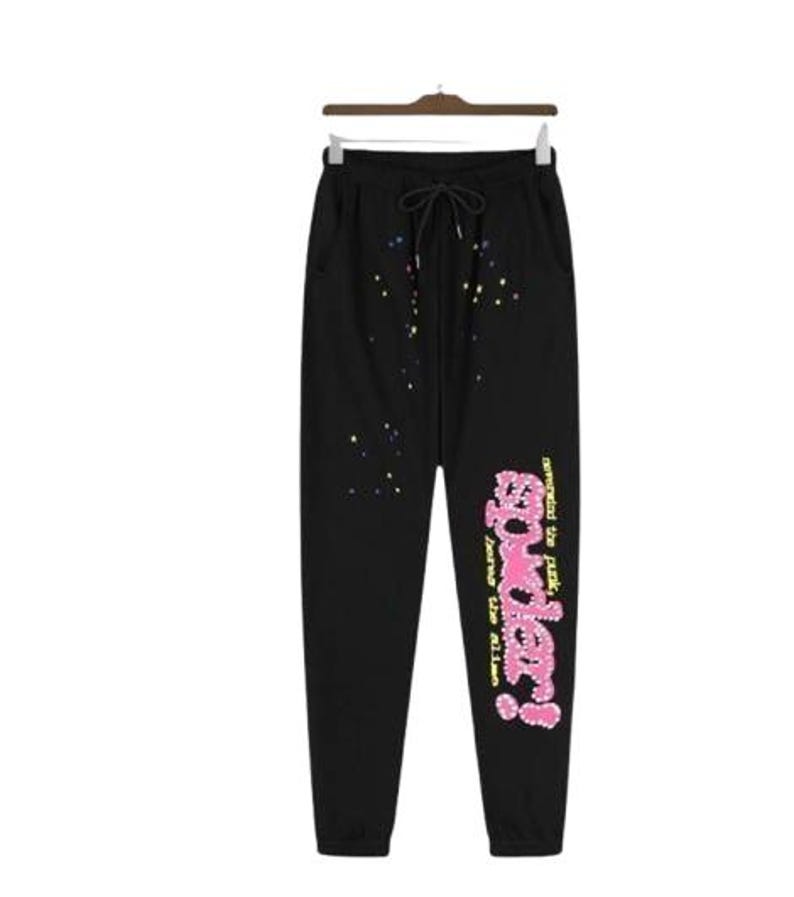 K&ouml;nnte beinhalten: Schwarze Jogginghose mit Kordelzug in der Taille, mehrfarbigen Farbspritzern im oberen Vorderbereich und einer gro&szlig;en rosa Grafik auf dem linken Bein mit der Aufschrift "sp5der!" sowie dem gelben Text "nevermind the punk, here the alien".