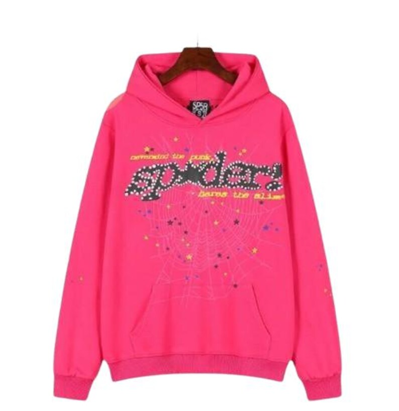 K&ouml;nnte beinhalten: Ein leuchtend pinkfarbener Kapuzenpullover mit einer gro&szlig;en schwarzen Grafik, die den Text "spider!", "demanded the punk" und "bares the slime" in Gelb zeigt. Das Design enth&auml;lt ein Spinnennetz-Muster mit kleinen bunten Sternen auf der Vorderseite.