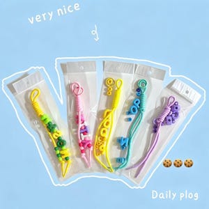 May include: Five individual clear plastic packages containing colorful beaded lanyards or keychains. The beads are in shades of yellow, pink, light blue, and purple, featuring various letter and shape designs. The text "very nice" and "Daily plog" appears.