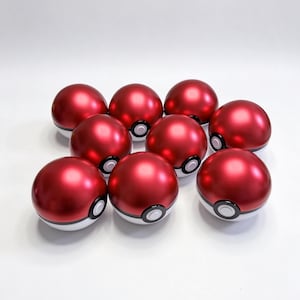 May include: A collection of nine spherical containers, each featuring a metallic red upper hemisphere and a white lower hemisphere. A circular black and white button detail is centered on the front of each sphere, mimicking a classic ball design.