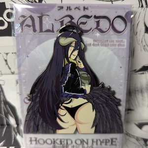 May include: A metal enamel pin featuring the anime character Albedo with long purple hair, horns, and dark wings, wearing a black jacket and black underwear. The backing card displays the text ALBEDO, Admire all you want... just don't forget your place, and HOOKED ON HYPE.