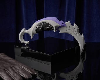 May include: A curved fantasy blade featuring a light grey blade with sharp, angular edges, a purple spine, and a black handle with a wrapped texture. The weapon includes a circular finger ring at the base and is displayed on a reflective black surface.