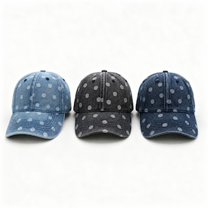 Peut inclure: Trois casquettes de baseball en tissu denim, chacune ornée d'un motif à pois blancs. Les casquettes sont alignées, présentant des délavages bleu clair, gris anthracite et bleu moyen, toutes dotées d'une visière courbée et d'un bouton.