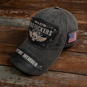 May include: A charcoal grey baseball cap featuring a black patch with the text 100% GITTER OLD FUCKERS CLUB and a winged skull graphic. The brim displays the text LIFETIME MEMBER, and a small American flag patch is attached to the side panel.