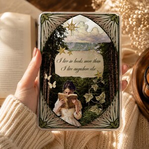 Peut inclure: Une coque de tablette transparente avec une illustration imprimée représentant une personne lisant un livre en forêt. Le texte indique, I live in books more than I live anywhere else. Le motif inclut une étoile, des papillons et du lierre.