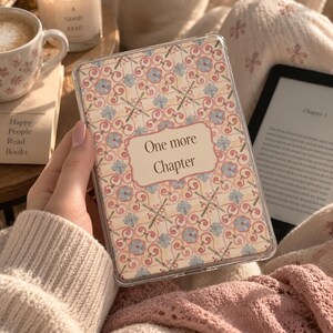 Puede incluir: Una funda protectora transparente para lector electrónico con un patrón repetitivo de flores azul claro y enredaderas rosas sobre un fondo crema, con una etiqueta rectangular central que contiene el texto negro One more Chapter.