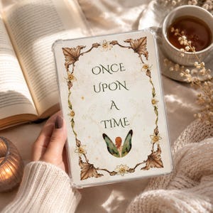 Könnte beinhalten: Eine transparente Tablethülle mit cremefarbenem Hintergrund und dem Text "ONCE UPON A TIME" in dunkelgrüner Schrift. Das Design zeigt einen dekorativen Rahmen aus braunen Blättern und weißen Blüten sowie ein Paar grüne Feenflügel am unteren Rand.