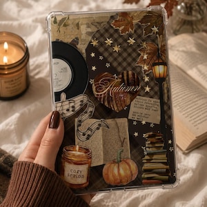May include: A clear tablet case featuring an autumn-themed collage with a vinyl record, musical notes, a heart-shaped leaf, a pumpkin, a stack of books, a street lamp, and text that reads Autumn, cozy season, and October is about trees revealing.