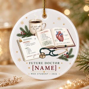 May include: A round white ceramic ornament featuring a coffee mug labeled med school nights big goals, an open textbook with medical notes and a heart illustration, a spiral notebook on pathophysiology, a stethoscope, and text reading FUTURE DOCTOR [NAME] MED STUDENT 2026.
