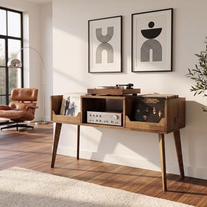 May include: A dark wood record console featuring a top surface for a turntable, a central shelf for an amplifier, and two side compartments for vinyl records. The console stands on four tapered legs and has a rectangular frame with open storage.
