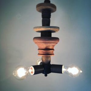 May include: A handcrafted wooden chandelier with three exposed light bulbs. The fixture features a dark wood base with a decorative, turned design and a light wood top. The Edison-style bulbs are lit, casting a warm glow.