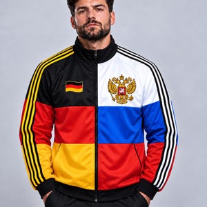 May include: A zip-up track jacket featuring a split design. The left side displays the black, red, and gold colours of the German flag with three yellow stripes on the sleeve. The right side features the white, blue, and red colours of the Russian flag with the golden double-headed eagle emblem and three white stripes on the sleeve.