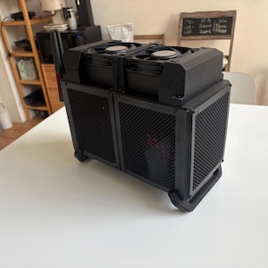 Op de afbeelding: Een zwarte computerbehuizing met een rechthoekig frame, voorzien van twee ventilatoren aan de bovenzijde en zijpanelen bedekt met een fijn metalen gaas. De structuur bevat een stevige basis met schuine voetjes en een verticale antenne achteraan.