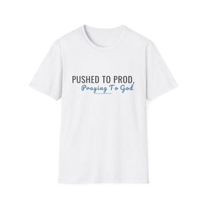 May include: A white short-sleeved t-shirt featuring the black text PUSHED TO PROD, followed by the blue cursive text Praying To God. The design is centered on the chest of the garment, which has a standard crew neckline and a simple, clean cut.