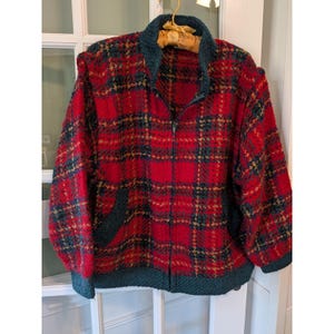 May include: A long-sleeve zip-up jacket featuring a red, dark green, and gold plaid pattern. The garment has a dark green textured collar, cuffs, and hem, with a full-length front zipper closure and two side pockets integrated into the plaid design.