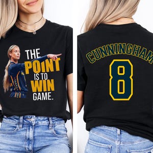 May include: A black t-shirt featuring a graphic of a basketball player pointing with the text THE POINT IS TO WIN GAME on the front. The back of the shirt displays the name CUNNINGHAM in an arch over the large number 8 in yellow and blue.