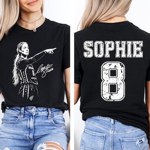 May include: A black short-sleeve t-shirt featuring a white graphic of a basketball player pointing on the front with a signature, and the name SOPHIE above the number 8 in a distressed white font on the back of the garment.