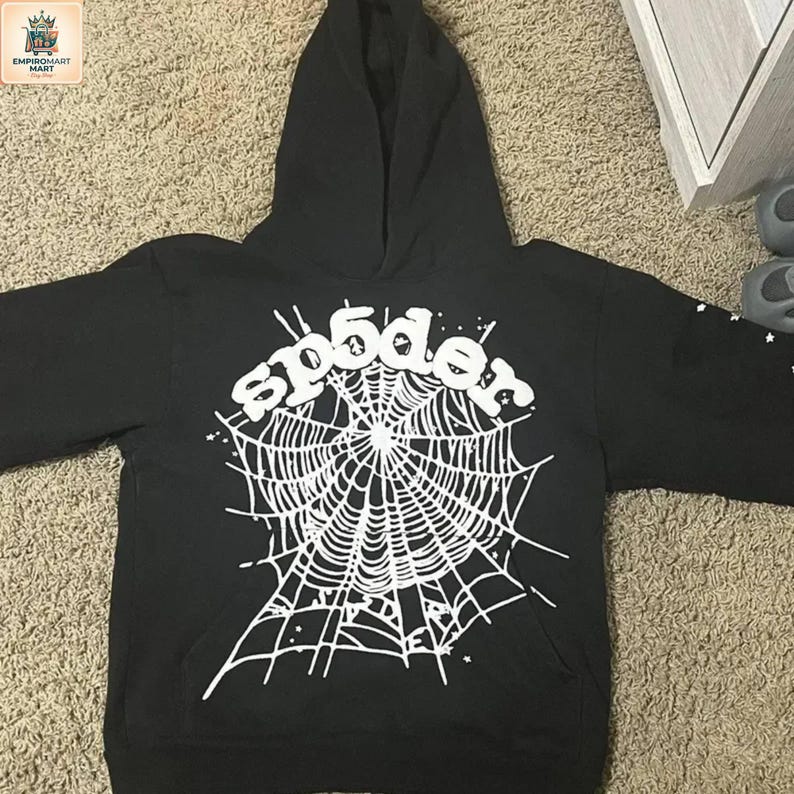 Puede incluir: Una sudadera con capucha negra que presenta un gran gr&aacute;fico blanco en la parte delantera. El dise&ntilde;o muestra un patr&oacute;n de telara&ntilde;a con el texto sp5der arqueado encima. Peque&ntilde;os detalles de estrellas blancas se esparcen por la red y la manga.