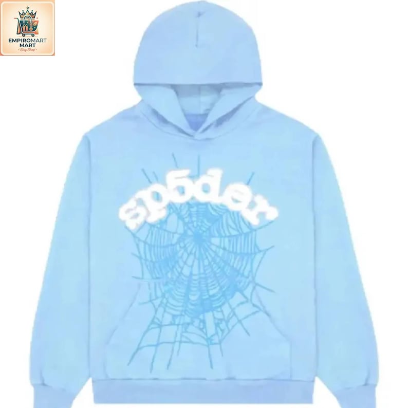 Puede incluir: Una sudadera con capucha de color azul claro que presenta un gran gr&aacute;fico blanco con la palabra sp5der arqueada sobre un dise&ntilde;o detallado de telara&ntilde;a en un tono azul m&aacute;s oscuro. La prenda incluye un bolsillo canguro, mangas largas y capucha.