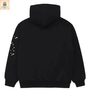Puede incluir: Una sudadera negra con capucha y mangas largas, que presenta una serie de peque&ntilde;os gr&aacute;ficos en forma de estrella blanca impresos a lo largo del borde exterior de la manga izquierda. La prenda incluye una capucha y pu&ntilde;os acanalados.