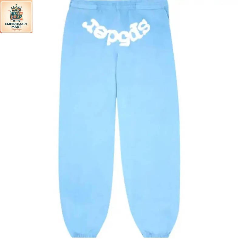 Puede incluir: Pantalones de ch&aacute;ndal azul claro con cintura el&aacute;stica y un estampado gr&aacute;fico blanco en la parte superior trasera. El texto 'spider' est&aacute; impreso en una fuente blanca redondeada y estilizada sobre el asiento del pantal&oacute;n de corte holgado.