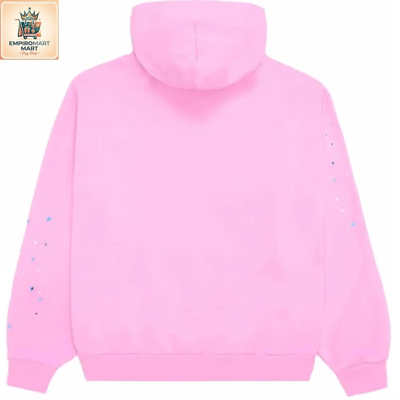 May include: A solid light pink hooded sweatshirt featuring long sleeves with small, scattered blue and white paint-like speckles on the outer arms. The garment has a standard hood, ribbed cuffs, and a ribbed hem, presented from a back view.