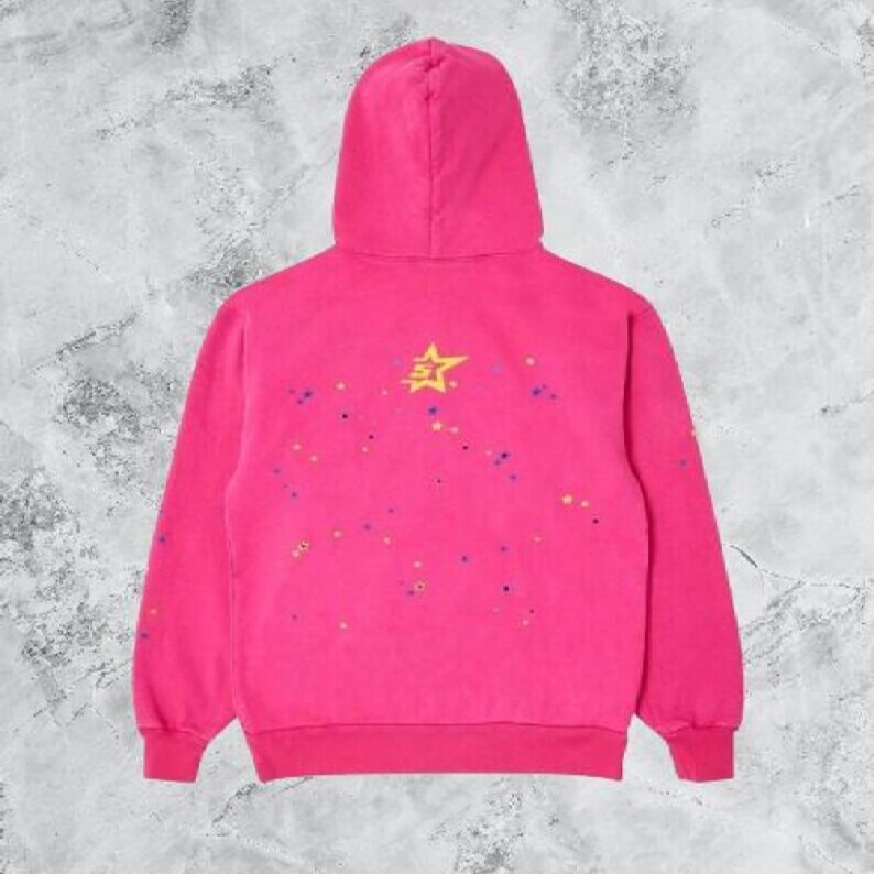 May include: A bright pink hooded sweatshirt featuring a yellow star graphic on the upper back. The back of the garment is decorated with small, scattered paint-like splatters in various colors including blue, yellow, and orange across the fabric.