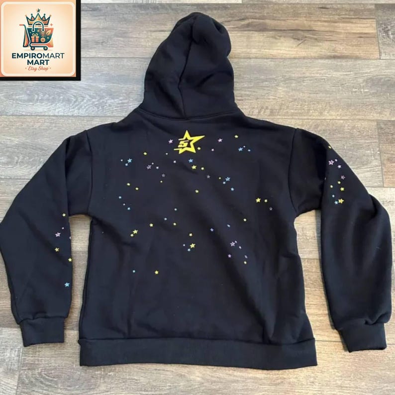 May include: A black hooded sweatshirt featuring a large yellow star graphic with the number 5 in the center on the upper back. The back and sleeves are decorated with a scattered pattern of small yellow, blue, and purple stars across the fabric.