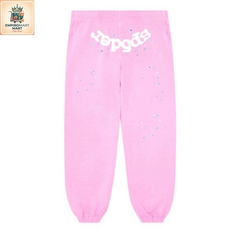 May include: Light pink sweatpants featuring a white graphic text logo that reads spider across the upper back area. The fabric is decorated with small, scattered blue and white paint-like speckles throughout the front surface of the garment.