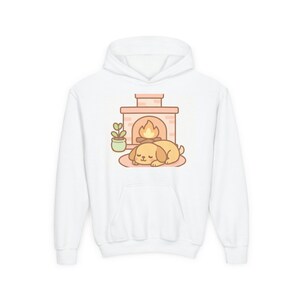 May include: A white hooded sweatshirt featuring a central graphic of a light brown puppy sleeping on a rug in front of a brick fireplace with a small potted plant to the left. The illustration uses soft pastel tones and simple line art.