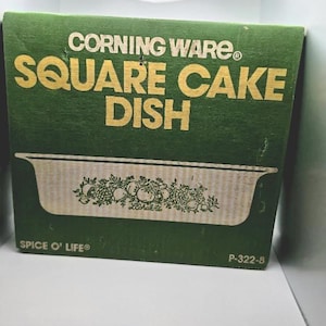 May include: A green cardboard box for a Corning Ware Square Cake Dish in the Spice O' Life pattern. The box features yellow text reading Corning Ware, Square Cake Dish, and Spice O' Life, with a graphic of the dish showing a vegetable motif.