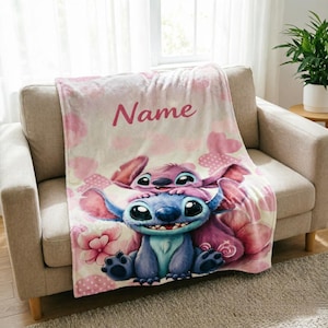Op de afbeelding: Een zachte pluche deken met een lichtroze achtergrond, witte stippen en roze hartjes. De deken toont een groot blauw alien-figuur met grote ogen en een kleiner roze alien-figuur op het hoofd, samen met het woord Name.