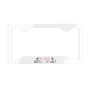 Puede incluir: Un marco de matrícula rectangular blanco con cuatro orificios de montaje. La parte inferior central presenta una ilustración vintage en blanco y negro de tres figuras y el texto rosa THE GIRLS en una fuente gótica dentada.