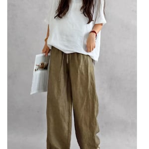 May include: A pair of olive green wide-leg trousers featuring an elasticated waistband with a drawstring closure, paired with a loose-fitting white short-sleeved top. The trousers have a relaxed, straight-leg silhouette and a textured fabric finish.