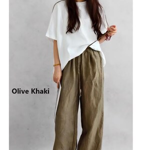May include: A pair of olive khaki wide-leg trousers with an elasticated waistband and a drawstring closure, paired with a plain white short-sleeved t-shirt. The text Olive Khaki is printed on the left side of the image in black lettering.