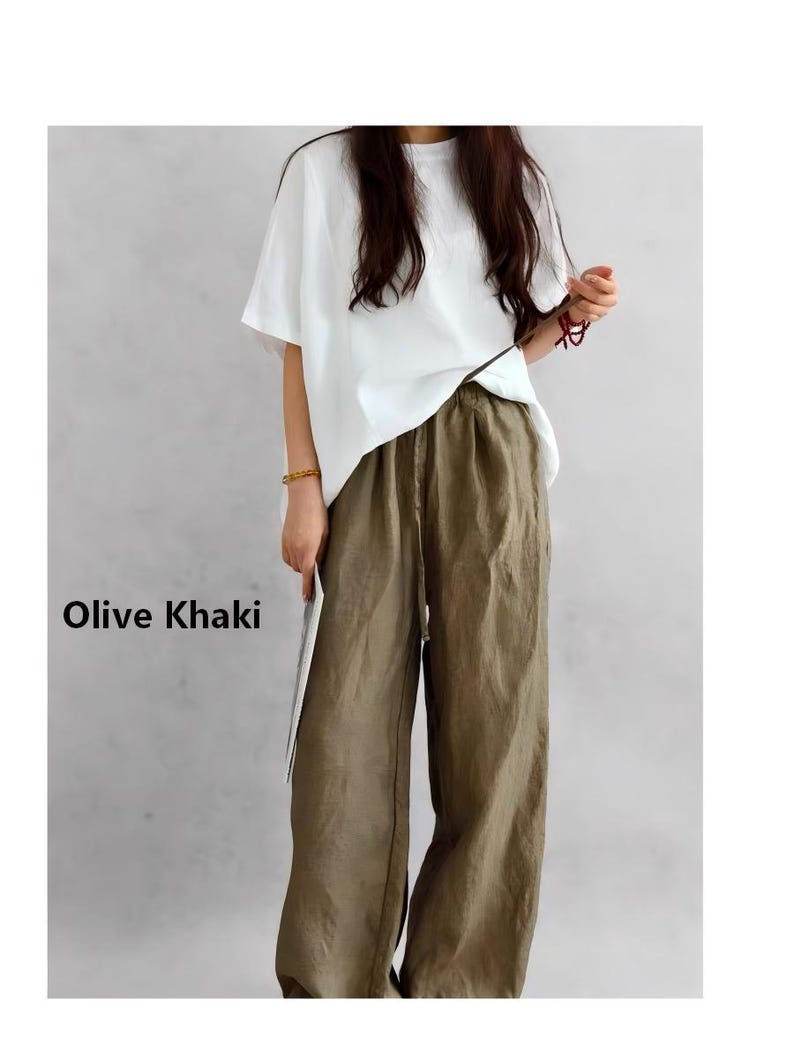May include: A pair of olive khaki wide-leg trousers with an elasticated waistband and a drawstring closure, paired with a plain white short-sleeved t-shirt. The text Olive Khaki is printed on the left side of the image in black lettering.