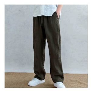 May include: Dark olive green trousers featuring a relaxed, straight-leg fit with an elasticated waistband and a drawstring closure. The trousers are paired with a white shirt and white trainers, showcasing a simple, functional design.
