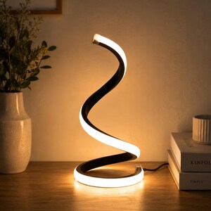 Puede incluir: Una lámpara de mesa en forma de espiral con un marco exterior negro y una tira de luz LED blanca continua que se enrolla hacia arriba en un diseño de doble curva, emitiendo una iluminación cálida y suave desde la base hasta la punta.