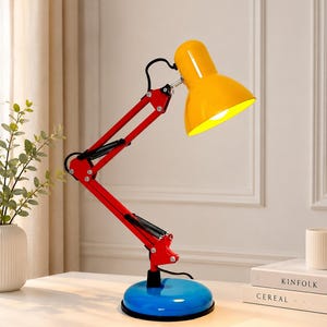 Peut inclure: Une lampe de bureau multicolore dotée d'un abat-jour conique jaune vif, d'un bras articulé rouge éclatant avec des ressorts noirs et d'une base circulaire bleue brillante. La lampe est posée sur une surface blanche près de livres et d'un stylo.