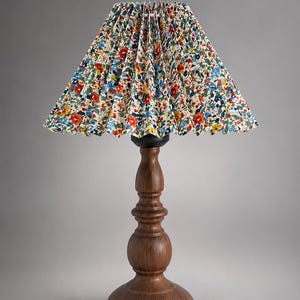 May include: A table lamp with a dark brown, turned wood base and a pleated, conical lampshade. The lampshade features a dense, colourful floral pattern with small red, blue, yellow, and green flowers against a cream-coloured background.