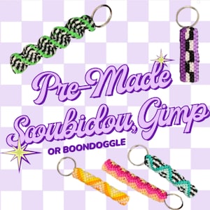 May include: Five plastic lacing keychains in various colors and patterns, including a green and black spiral, a purple and black checkerboard, a yellow and orange spiral, a pink and orange spiral, and a teal and black spiral, with text reading Pre-Made Scoubidou, Gimp OR BOONDOGGLE.