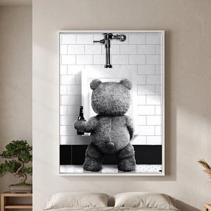 May include: A framed wall art print featuring a black and white image of a teddy bear standing at a white tiled urinal while holding a dark glass bottle. The bear is viewed from behind, positioned against a wall with white subway tiles and black trim.