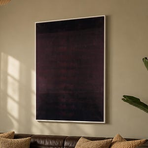 May include: A large rectangular wall art piece featuring a deep dark purple abstract design in a thin white frame, displayed above a tufted dark brown leather sofa with four textured tan throw pillows and a glass-topped coffee table.