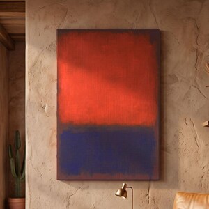 May include: A rectangular wall art piece featuring a large horizontal block of vibrant red over a deep blue section. The painting is displayed on a textured beige wall above a wooden side table with a lamp and a tan leather armchair with a throw.